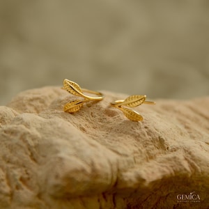 Può includere: Un paio di ear cuff color oro a forma di foglie delicate e ramificate con venature testurizzate. Ogni pezzo presenta due piccoli motivi a foglia appuntita che si estendono da uno stelo centrale, progettati per avvolgere il bordo dell'orecchio.