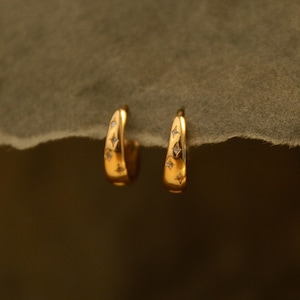 May include: A pair of gold-colored hoop earrings. Each earring features a series of small, sparkling diamond-like accents. The earrings have a smooth, polished finish and a curved design, creating a simple yet elegant look.