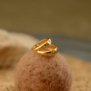 May include: A pair of gold-colored hoop earrings with star-shaped cutouts and small, clear gemstones. The earrings are displayed on a textured, brown surface, with a soft, blurred background.