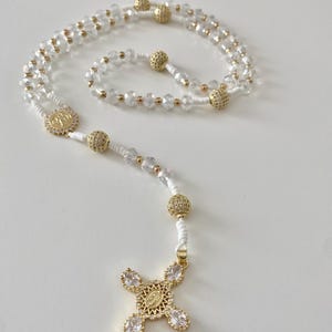 Christian rosary in white and gold beads, medal of St. Benedict in gold metal, cross with the Holy Virgin Mary