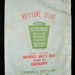 May include: A white fabric seed bag with red and green text. The bag is labeled "KEYSTONE SEEDS" and features the text "CORNELI KEYSTONE (SELECTED) CLEANED TESTED SEEDS TRADE MARK ONE POUND IMPROVED HALE'S BEST CROWN SET CANTALOUPE CORNELI SEED CO. ST. LOUIS, MO."