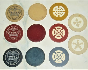 May include: Ten round poker chips with different designs.  Three chips feature a crown with the word "CROWN" below it.  Three chips feature a white cross design on a red, blue, or yellow background.  Two chips feature a white snowflake or clover design on a beige background.  One chip is solid red and one chip is solid blue.