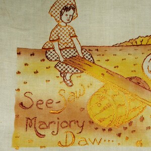May include: A light-colored fabric panel featuring an embroidered illustration of a child in a checkered outfit sitting on a seesaw. The design includes a wooden barrel support and the embroidered text "See-Saw Marjory Daw..." in brown thread.