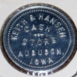 May include: A silver token with the text "Keith & Hansen Cash Store, Audubon, Iowa" around the edge.