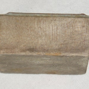 May include: A rectangular block of wood with a slightly rounded top and a metal strip along the top edge. The wood has a natural, weathered finish.