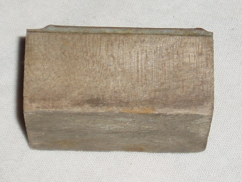 May include: A rectangular block of wood with a slightly rounded top and a metal strip along the top edge. The wood has a natural, weathered finish.