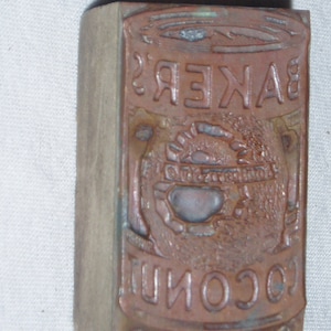 May include: A vintage wooden printing block with the text "BAKER'S COCONUT" in raised letters. The block is worn and has a brown patina.