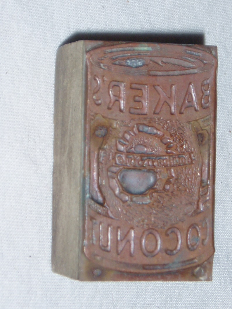 May include: A vintage wooden printing block with the text "BAKER'S COCONUT" in raised letters. The block is worn and has a brown patina.