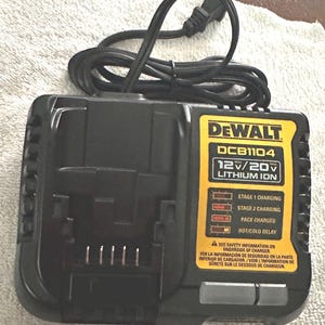 May include: A black and yellow DeWalt DCB1104 12V/20V Lithium Ion battery charger. The charger has a black power cord and displays charging stages. The text on the charger includes safety information.