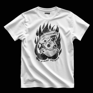 Puede incluir: Camiseta blanca con una ilustración en blanco y negro de un conejo y una gallina en llamas. El texto "RAGE AGAINST SPECIESISM" está impreso debajo. La camiseta tiene cuello redondo y mangas cortas.