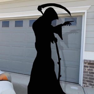 May include: A large black silhouette of the Grim Reaper, holding a scythe and pointing. The figure is positioned in front of a gray garage door, creating a spooky Halloween decoration.
