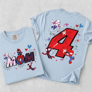 May include: Two light blue t-shirts with Spider-Man graphics. One shirt features the word "MOM" with a spider web design, and the other has a large red number "4" with a spider web design. Both shirts have Spider-Man characters.