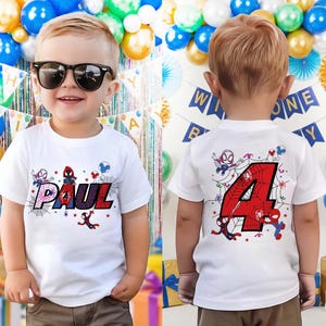 May include: A white t-shirt featuring the name "PAUL" in a colorful, web-themed design with Spider-Man characters. The back of the shirt displays a large red number "4" with a spiderweb design and more Spider-Man graphics. The shirt is for a child.