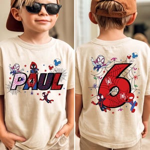 May include: Beige t-shirt featuring a colorful Spider-Man design. The front displays the name "PAUL" in a webbed font, with Spider-Man characters and stars. The back shows a large red number "6" with Spider-Man graphics, ideal for a birthday.
