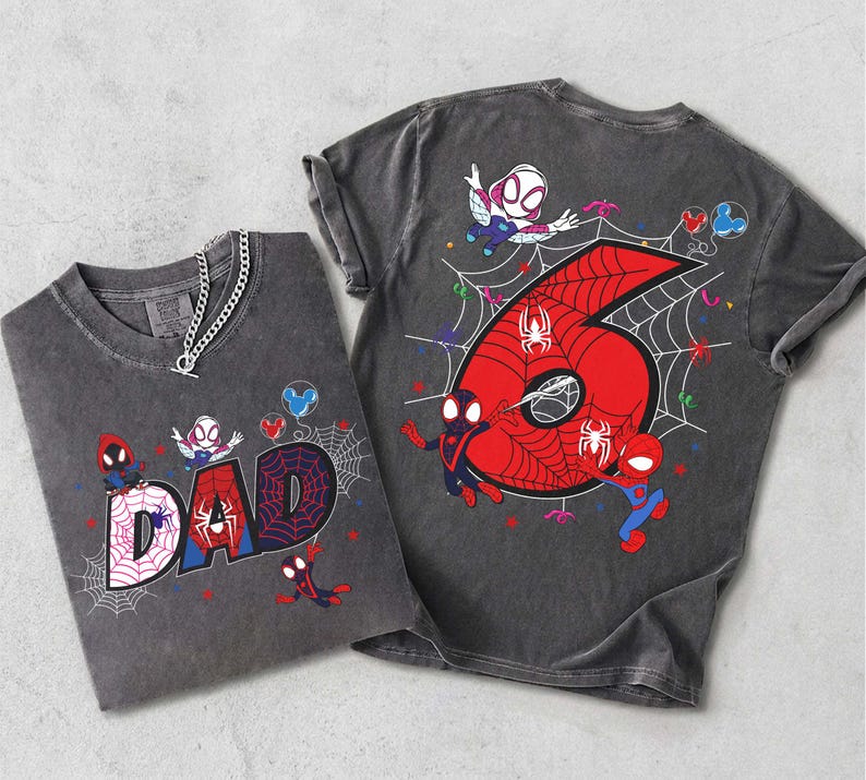 May include: Two gray t-shirts with Spiderman graphics. One shirt says "DAD" with a spiderweb design. The other shirt has a large red number "6" with a spiderweb and Spiderman characters. Both shirts have a chain necklace.