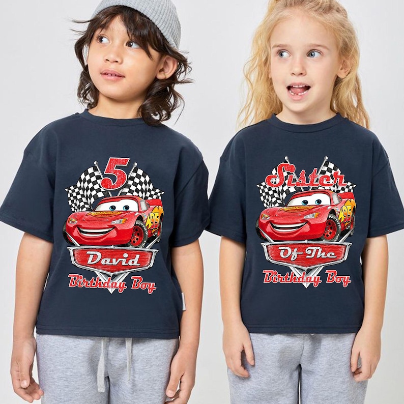 Puede incluir: Dos camisetas azul marino con un dise&ntilde;o de coche de carreras rojo de dibujos animados. Una camiseta dice "5" y "David Birthday Boy", la otra dice "Sister Of The Birthday Boy". Ambas tienen un dise&ntilde;o de bandera a cuadros.