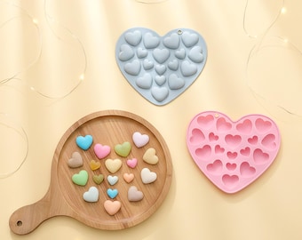 May include: A light blue heart-shaped silicone mold, a pink heart-shaped silicone mold, and a round wooden serving board featuring an assortment of small, multi-colored heart-shaped items in shades of blue, pink, green, yellow, and beige.