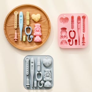 May include: A wooden tray and two silicone moulds filled with medical-themed shapes. The tray holds yellow, blue, and pink medical tools. The pink mould features a nurse, stethoscope, and thermometer. The grey mould has similar shapes.