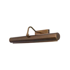 Puede incluir: Una lámpara de bronce para cuadros con un brazo curvo y un soporte de pared rectangular. La luz cilíndrica tiene un extremo redondeado. El accesorio está diseñado para iluminar obras de arte y está montado sobre un fondo blanco.