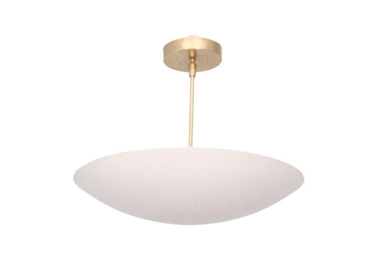 May include: A modern white pendant light with a brass-colored canopy and stem. The light fixture has a large, oval-shaped shade, and is suspended from the ceiling. The design is minimalist and suitable for various interior styles.