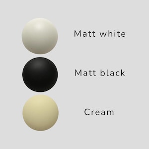 May include: Three matte spheres in a row: white, black, and cream. The text next to each sphere reads "Matt white", "Matt black", and "Cream". The spheres are evenly spaced against a light gray background.
