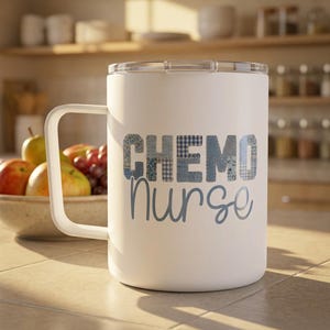 May include: White travel mug with a handle and a clear lid. The mug features the words "Chemo Nurse" in blue lettering. The word "Chemo" is made of a patchwork design. A bowl of fruit is in the background.