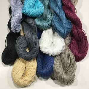 May include: A collection of 12 skeins of linen yarn in various colors, including teal, gray, white, beige, black, navy, and burgundy.