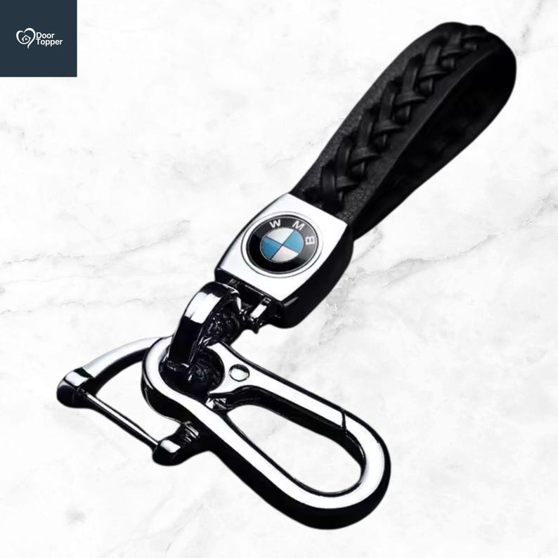 May include: Black leather braided keychain with a silver clasp and a BMW logo. The keychain has a black leather strap and a metal clasp for attaching keys. The BMW logo is in the centre of the metal plate.
