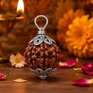 Peut inclure: Un pendentif en perle de rudraksha marron, sphérique et texturé, doté de capuchons en métal argenté en haut et en bas. Le capuchon supérieur comprend une bélière circulaire argentée pour la suspension, et la perle présente une surface naturelle.