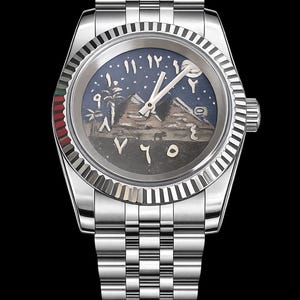 May include: A stainless steel wristwatch with a detailed dial featuring an Egyptian landscape with pyramids, palm trees, and Arabic numerals. The watch has a silver band and a fluted bezel with red and green accents.