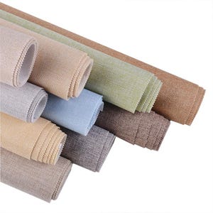 May include: Assortment of rolled fabric in various neutral colors, including beige, gray, blue, and brown. The fabric has a textured appearance, suggesting a woven material. The rolls are neatly arranged, showcasing the different shades and textures.