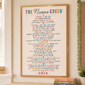 May include: A framed wall art print featuring the Nicene Creed text in a multi-colored font on a white background. The text is arranged in a central column with small heart icons separating sections, ending with the word AMEN in red letters.