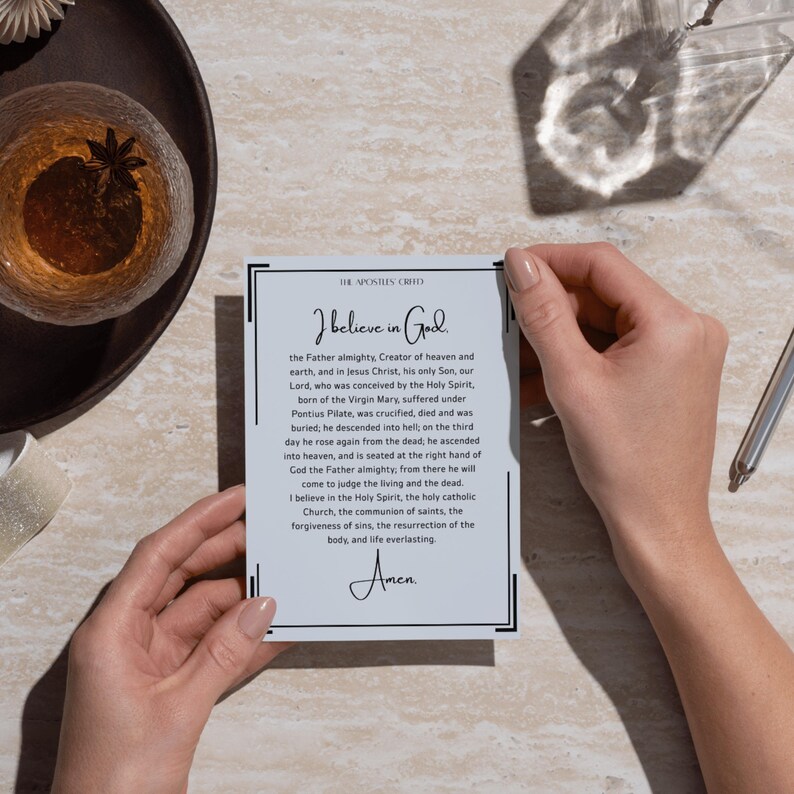 May include: A rectangular white card featuring the text of The Apostles' Creed in black ink. The card has a thin black border and includes the title, the full prayer text starting with I believe in God, and the word Amen at the bottom in script font.