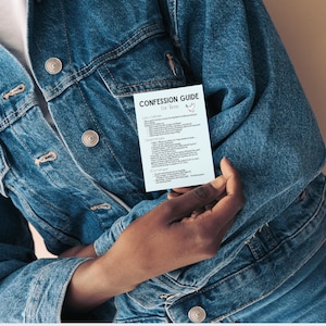 May include: A light blue rectangular card titled CONFESSION GUIDE For Kids with black text and a small dove illustration. The card is held against a blue denim jacket featuring silver metal buttons, a chest pocket, and visible seams.