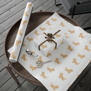 May include: White wrapping paper with a repeating pattern of light brown dachshund dogs. A wrapped gift box with a brown ribbon, a roll of matching paper, scissors, and tape are on a wooden table.