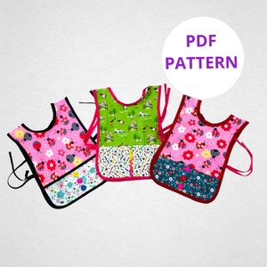 May include: Three pink and green fabric bibs with different patterns. The bibs have a pocket on the front and adjustable straps. The text "PDF PATTERN" is in a white circle with a purple outline.