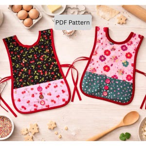 May include: Two colorful bib aprons with red trim and ties. One apron has a black background with cherry print, the other has a pink floral pattern. Both have a pink gingham bottom and red buttons. The text "PDF Pattern" is visible.