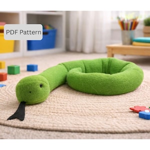 Puede incluir: Un juguete de peluche con forma de serpiente verde con lengua negra y ojos negros pequeños, enrollado sobre una alfombra beige. Las palabras "PDF Pattern" están en un cuadro blanco en la esquina superior izquierda. Juguete para niños.