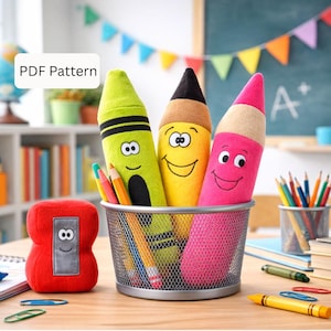 May include: A whimsical classroom scene features plush crayon and pencil-shaped toys with smiling faces, held in a metal mesh container. A red number 8 plush toy and colorful pencils are also present. The image includes the text "PDF Pattern".