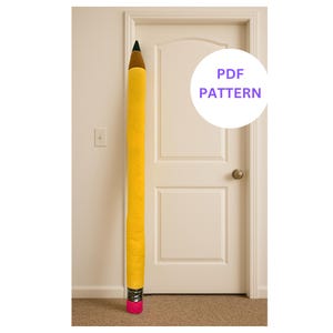 Può includere: Un grande fermaporta a forma di matita gialla con punta marrone e gomma rosa. Il fermaporta è posizionato verticalmente contro una porta bianca. Il testo "PDF PATTERN" è in un cerchio bianco.