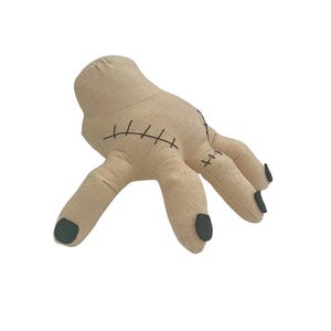 May include: A beige plush hand with black stitched details and black painted fingernails. The hand has a stitched seam design and is in a relaxed pose. The fingers are slightly curved, and the thumb is angled.
