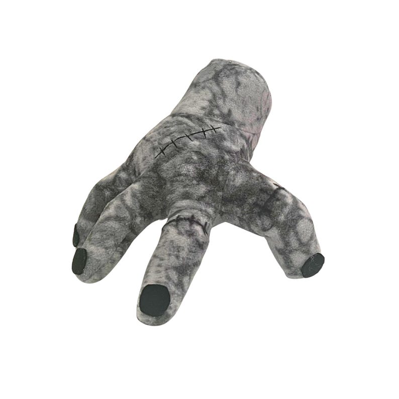 May include: A plush, gray hand with black fingertips and stitched details. The hand is a novelty item, likely a prop or decorative piece, with a textured appearance and a slightly eerie aesthetic.