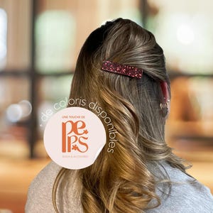May include: A burgundy rectangular hair clip with glitter is placed in the hair. The hair is long and wavy, with highlights. A sticker with the text "Une touche de PePs Bijoux & Accessoires" is visible.