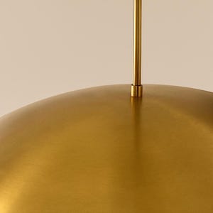 May include: A gold-colored, dome-shaped pendant light fixture. The light has a brushed metal finish and a slender, gold-colored rod extending upwards. The fixture is suspended from the ceiling, offering a modern aesthetic.