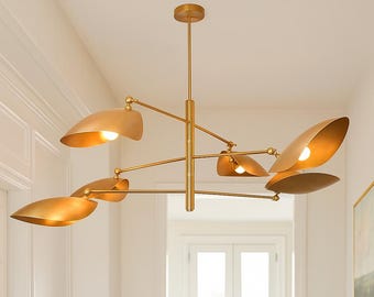May include: A modern gold-toned chandelier with six leaf-shaped shades. The light fixture is suspended from the ceiling and features adjustable arms. Each shade houses a light bulb, creating a warm, inviting glow. The design is sleek and contemporary.