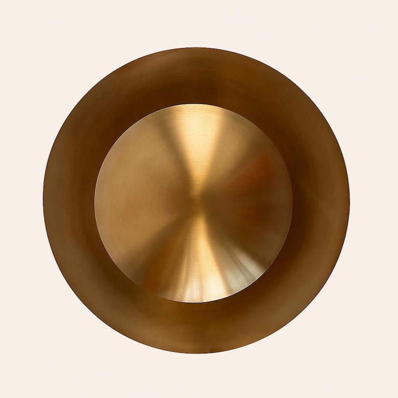 May include: A circular, two-toned metal object with a gold-colored center and a bronze-colored outer ring. The object has a reflective surface, creating highlights and shadows. The design is simple and modern, suitable for home decor.