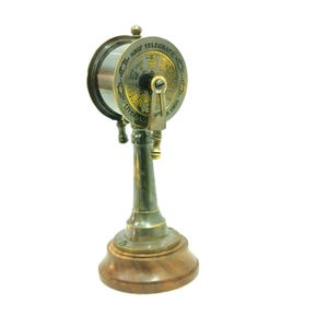 Può includere: Un telegrafo navale in ottone vintage su una base di legno. Il telegrafo ha un quadrante circolare con testo e una leva. La base è di colore marrone scuro e il metallo ha una finitura calda e antica.