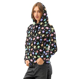 Könnte beinhalten: Schwarzer Kapuzenpullover mit einem farbenfrohen Muster aus cartoonartigen Formen und Sternen. Das Design weist Pastellfarben wie Rosa, Blau, Gelb und Grün auf. Der Hoodie hat einen Kordelzug und eine Vordertasche.