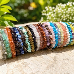 Può includere: Una collezione di braccialetti elastici composti da varie scaglie di pietre preziose colorate e levigate. I braccialetti sono disposti in fila orizzontale, mostrando uno spettro di colori che include bianco, verde, arancione, blu, marrone, nero e giallo.