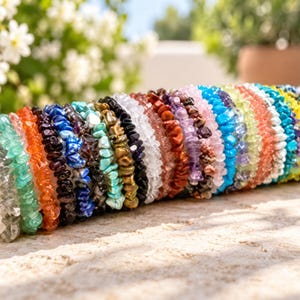 Könnte beinhalten: Eine Sammlung mehrerer Stretch-Armbänder aus verschiedenen bunten, getrommelten Edelstein-Splittern. Die Armbänder weisen eine breite Palette an Farben auf, darunter transparent, grün, orange, dunkelviolett, blau, schwarz, türkis, gold, weiß, rot und gelb.